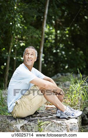 Picture - Mid adult man sitting on rock. Fotosearch