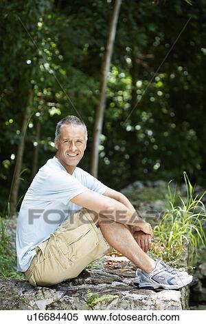 Stock Photography - Mid adult man sitting on rock. Fotosearch