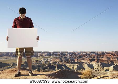 Young man holding blank piece of paper on rocky landscape View Large Photo Image Stock Image - Young man holding blank piece of paper on rocky landscape. Fotosearch
