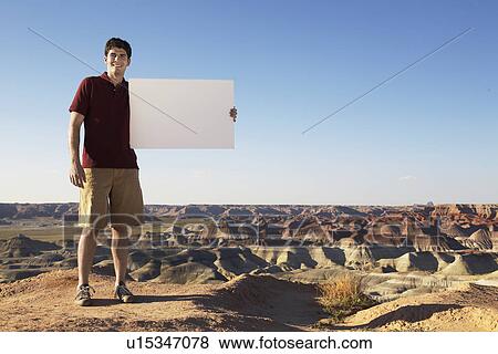 Young man holding blank piece of paper on rocky landscape View Large Photo Image Stock Photo - Young man holding blank piece of paper on rocky landscape. Fotosearch