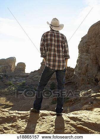 Young man in cowboy hat standing on cliff, rear view View Large Photo Image Stock Photo - Young man in cowboy hat standing on cliff, rear view. Fotosearch