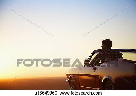 Stock Image - Young man looking at sunset in convertible, Arizona, USA. Fotosearch