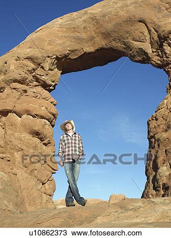 Stock Image - Young man standing under arched rock. Fotosearch