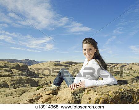 Stock Photo - Young woman sitting on rock, portrait, rear view. Fotosearch