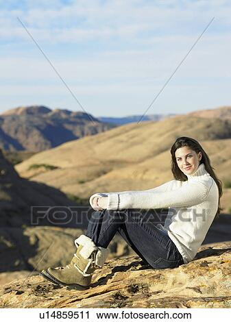 Stock Image - Young woman sitting on rocky hill, portrait. Fotosearch