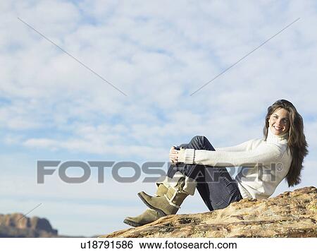 Stock Photograph - Young woman sitting on rocky hill, portrait. Fotosearch