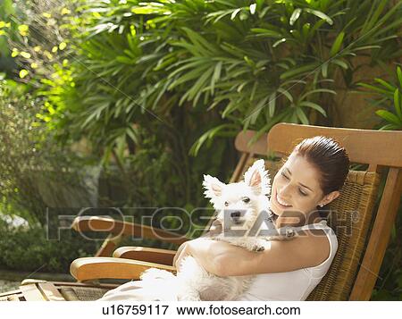 Young woman sitting on garden chair and holding poodle View Large Photo Image Stock Photo - Young woman sitting on garden chair and holding poodle. Fotosearch