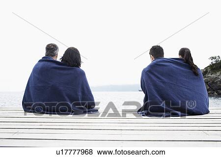 Stock Photo - Mature and young couple wrapped in a blanket on jetty. Fotosearch