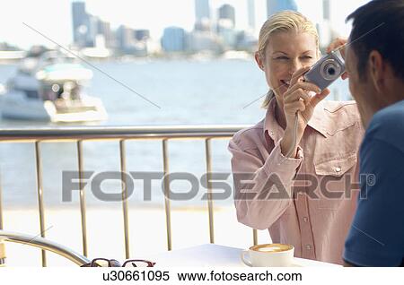 Stock Photography - Woman taking photograph of man at waterfront. Fotosearch