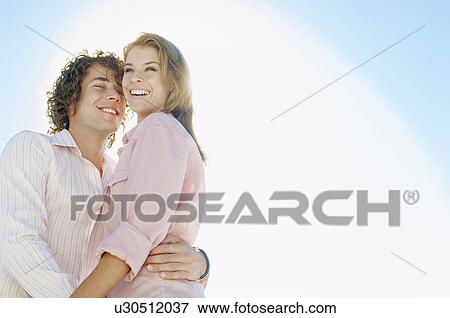 Stock Photo - Young couple against clear sky (portrait, low angle view). Fotosearch