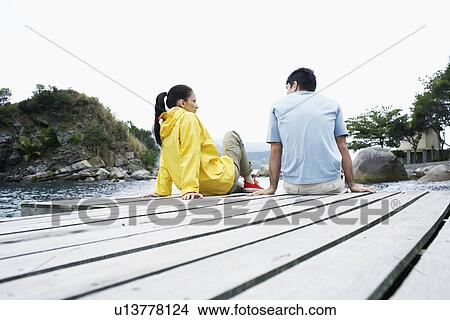 Young couple sitting on deck and talking (low angle view) View Large Photo Image Picture - Young couple sitting on deck and talking (low angle view). Fotosearch