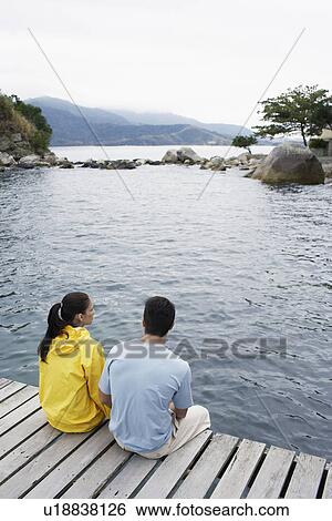 Young couple sitting on jetty and looking at view View Large Photo Image Stock Photograph - Young couple sitting on jetty and looking at view. Fotosearch