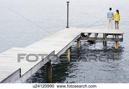 Young couple standing on jetty and looking at view View Large Photo Image Stock Image - Young couple standing on jetty and looking at view. Fotosearch