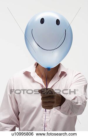 Stock Photograph - Man holding balloon with smiley face in front of his face. Fotosearch