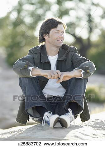 Mid adult man sitting on rock, portrait View Large Photo Image Stock Image - Mid adult man sitting on rock, portrait. Fotosearch