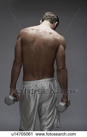 Stock Image - Mid adult man holding dumbbells (rear view). Fotosearch