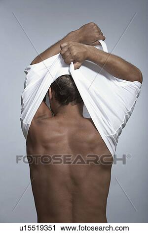 Stock Image - Mid adult man pulling T-shirt off. Fotosearch