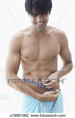 Stock Image - Young man measuring waist. Fotosearch