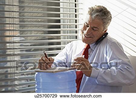 Stock Photo - Businessman on Phone by Water Cooler. Fotosearch