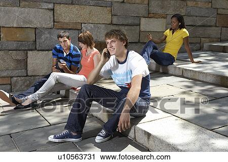 Stock Image - Four teenagers using mobile phones and MP3 players. Fotosearch