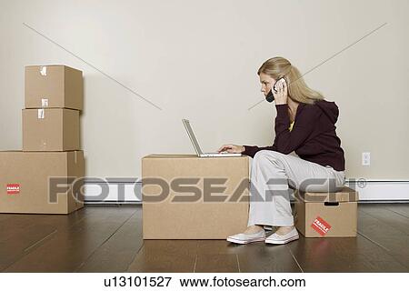 Mature woman using laptop and mobile phone on cardboard box View Large Photo Image Stock Photo - Mature woman using laptop and mobile phone on cardboard box. Fotosearch