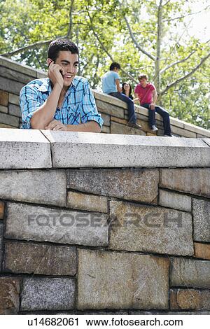 Stock Image - Teenage boy on mobile phone, two people in background. Fotosearch
