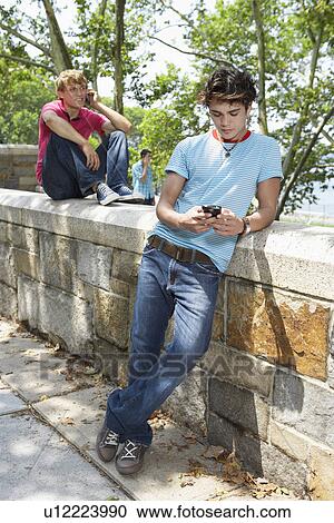 Stock Image - Teenage boy with mobile phone, friends in background. Fotosearch