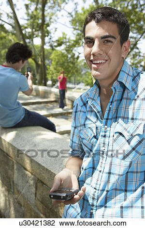 Teenage boy with mobile phone, friends in background View Large Photo Image Stock Image - Teenage boy with mobile phone, friends in background. Fotosearch
