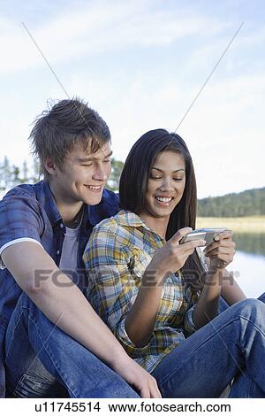 Picture - Teenage couple using mobile phone by lake. Fotosearch