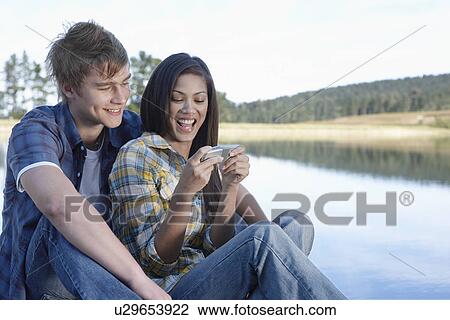 Teenage couple using mobile phone by lake View Large Photo Image Stock Image - Teenage couple using mobile phone by lake. Fotosearch