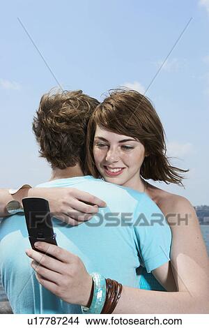 Teenage girl hugging boyfriend and using mobile phone View Large Photo Image Picture - Teenage girl hugging boyfriend and using mobile phone. Fotosearch