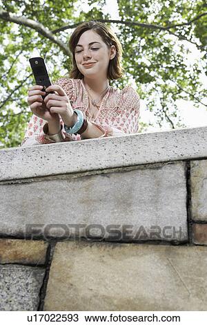 Stock Image - Teenage girl using mobile phone (low angle view). Fotosearch