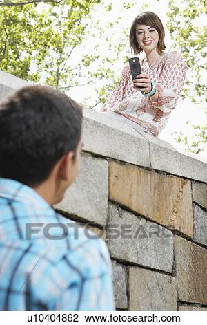 Teenage girl with camera phone taking photograph of young man (low angle view) View Large Photo Image Stock Image - Teenage girl with camera phone taking photograph of young man (low angle view). Fotosearch