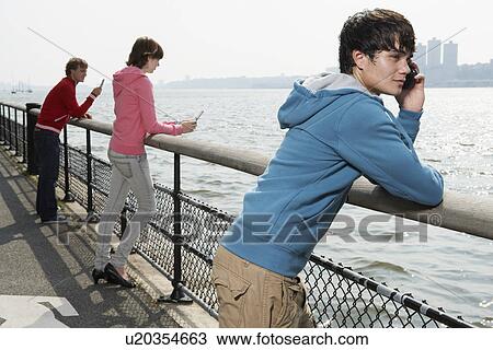 Three teenagers using mobile phone at waterfront View Large Photo Image Stock Image - Three teenagers using mobile phone at waterfront. Fotosearch