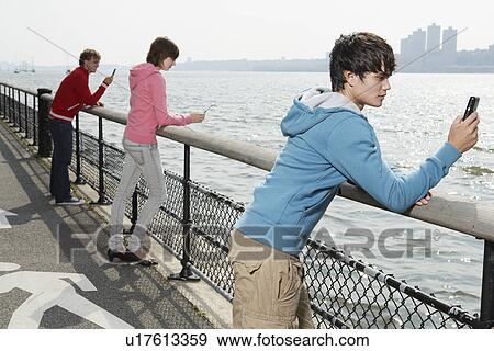 Three teenagers using mobile phone at waterfront View Large Photo Image Stock Photo - Three teenagers using mobile phone at waterfront. Fotosearch
