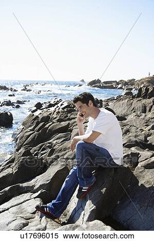 Young man on mobile phone by sea View Large Photo Image Stock Photography - Young man on mobile phone by sea. Fotosearch