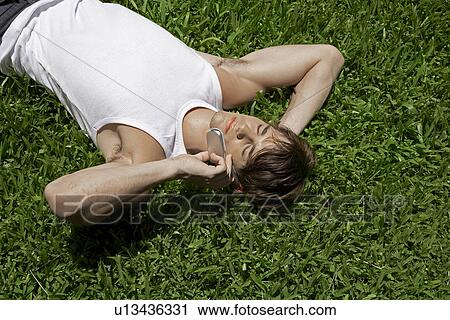 Stock Image - Young Man Using Mobile Phone on Lawn. Fotosearch