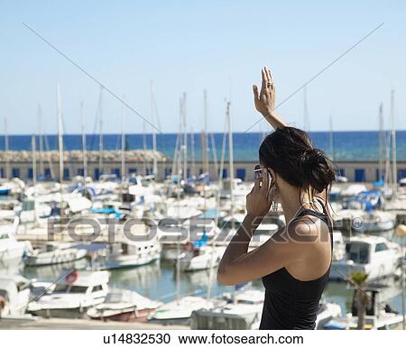 Stock Image - Young Woman Waving and Talking on Mobile Phone . Fotosearch