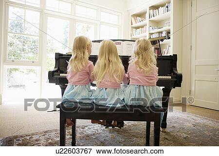 Triplets playing piano in living room (rear view) View Large Photo Image Stock Photo - Triplets playing piano in living room (rear view). Fotosearch