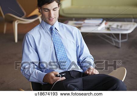 Stock Image - Young businessman listening to MP3 player. Fotosearch