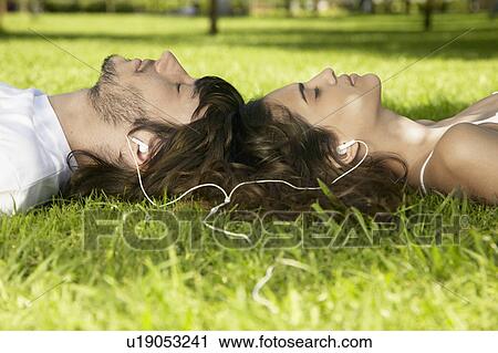 Stock Image - Young couple sharing MP3 player on grass. Fotosearch