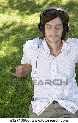 Young man listening to headphones on grass View Large Photo Image Stock Photograph - Young man listening to headphones on grass. Fotosearch