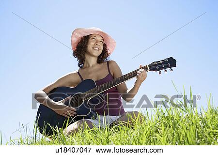 Young woman playing guitar on grass (low angle view) View Large Photo Image Stock Photo - Young woman playing guitar on grass (low angle view). Fotosearch