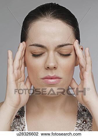 Stock Image - Young woman rubbing temples. Fotosearch