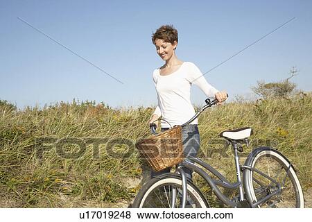 Stock Photo - Mid adult woman with bicycle walking on path. Fotosearch