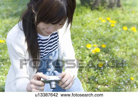 Woman smiling and holding a digital camera on lawn, front view, Japan View Large Photo Image Stock Image - Woman smiling and holding a digital camera on lawn, front view, Japan. Fotosearch