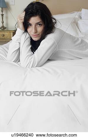 Stock Image - Young woman lying on bed (portrait, focus on background). Fotosearch