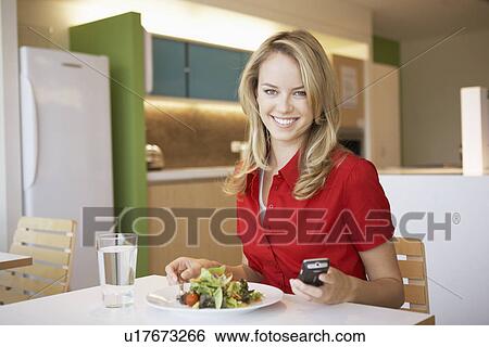 Young woman using cell phone while having lunch View Large Photo Image Stock Photograph - Young woman using cell phone while having lunch. Fotosearch