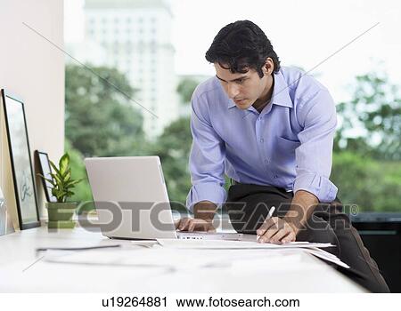 Businessman sitting on table and using laptop View Large Photo Image Stock Image - Businessman sitting on table and using laptop. Fotosearch