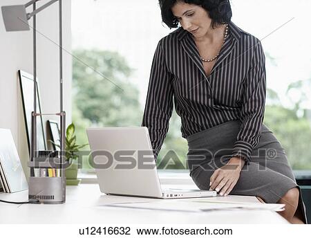 Businesswoman sitting on table and using laptop View Large Photo Image Stock Image - Businesswoman sitting on table and using laptop. Fotosearch